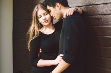 Siyah elbiseli, ahşap bir duvarın arkasında poz veren çok kültürlü bir çift. Türk erkek ve Kafkas kız buluşmaları ve aşkları. Müslüman adam ve sedye kadın birlikte..