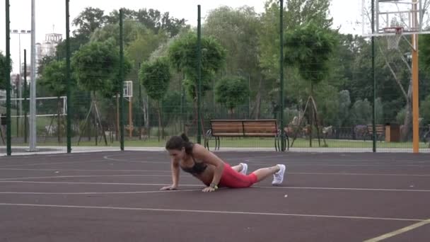 Beautiful Energetic Fitness Girl Haciendo ejercicios de Jack Burpee. Hacer ejercicio en una cancha de baloncesto al aire libre vallada. Hermosa chica de fitness haciendo burpee y push-UPS durante el entrenamiento en el estadio — Vídeo de stock