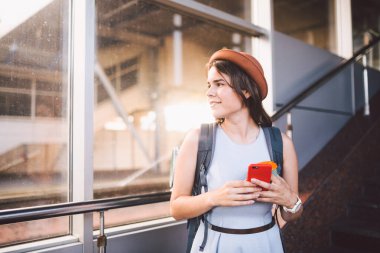 Tren istasyonunda dururken akıllı telefon kullanan bir kadın. Seyahat ve tatil konsepti. Tema Taşımacılık ve Seyahat. Şapkalı turist kadın tren ya da uçak biletini kontrol ediyor..