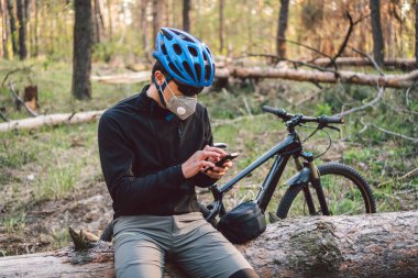Ormanda kirlilik maskesi takan bisikletçi. Solunum cihazındaki 2.5 numaralı filtreyle parktaki bisikletli genç adam. Covid 19 Karantina Spor. Grip salgını, toz alerjisi, koruma virüsü. Covid 19 virüs konsepti