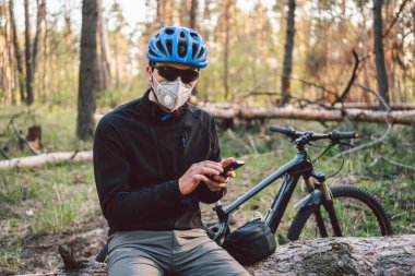 Ormanda kirlilik maskesi takan bisikletçi. Solunum cihazındaki 2.5 numaralı filtreyle parktaki bisikletli genç adam. Covid 19 Karantina Spor. Grip salgını, toz alerjisi, koruma virüsü. Covid 19 virüs konsepti