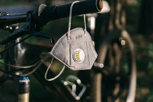 Close up PM2.5 mask or N95 mask. Air pollution pm2.5 concept. For protection pm 2.5 and coronavirus COVID 19. A carbon filter respirator hangs on the handlebars of a bicycle in a forest.