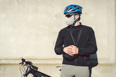 Portre erkek bisikletçi, gri beton duvarın yanında koruyucu solunum cihazıyla 2,5 numaralı filtrede. İnsan solunum organlarını tozdan ve havada asılı kalmış parçacıklardan, bulaşıcı hastalıklardan korur.