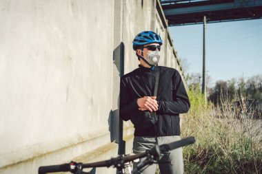 Portre erkek bisikletçi, gri beton duvarın yanında koruyucu solunum cihazıyla 2,5 numaralı filtrede. İnsan solunum organlarını tozdan ve havada asılı kalmış parçacıklardan, bulaşıcı hastalıklardan korur.