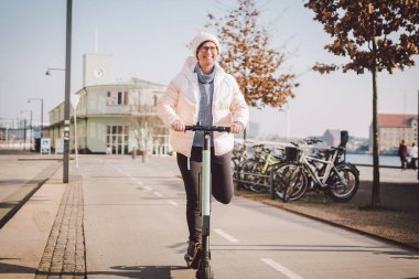 Bir kadın elektrikli scooter kiraladı ve Kopenhag, Danimarka 'da güneşli bir kış günü ata binmeyi planlıyor. Ekolojik temizlik nakil teması. Şehir ulaşımının yeni hızlı görüntüsü elektrikli kaykay.