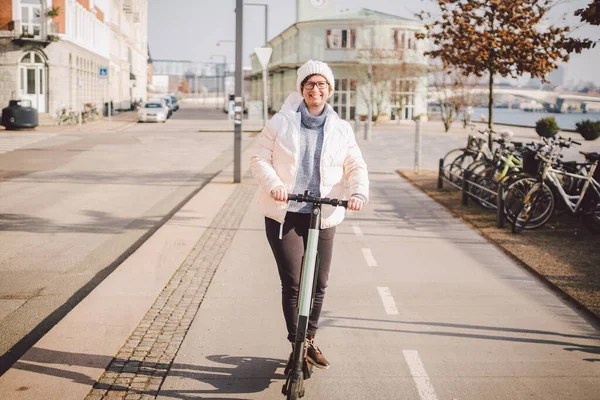 A woman has rented an electric scooter and is planning to ride on a sunny winter day in Denmark, Copenhagen. Ecological clean transport theme. New quick view of urban transport electric skateboard.
