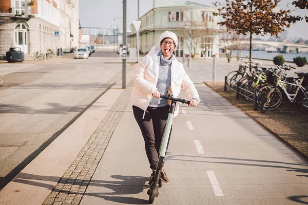 Young woman riding an electric scooter on bike path in copenhagen, modern girl, new generation, electric transport in city, ecology and ecological transport. Woman renting electric skateboard in city.