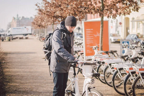 Man taking bike in bike sharing. Man take city bicycle vacation at the parking. Public electric bikes for rent parked in Copenhagen, Denmark. Save CO2 and Green energy. Person and cycle in europe.