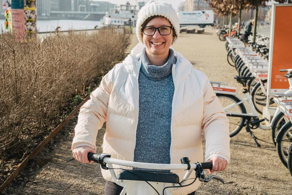 girl renting city bike from bike stand in Copenhagen, Denmark. Beautiful woman taking bicycle for rent. Happy woman unlocking bike share on street. Woman taking public city bicycle.