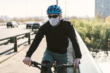 Motosikletli, N95 maskeli, üstü örtülü bir şehirde. Hava kirliliği. Endüstriyel şehir. Tozdan maskeli adam. Solunum cihazındaki adam 2.5 temalı Covid 19. Sis, kirlenmiş zehirli hava, solunum hastalıkları.