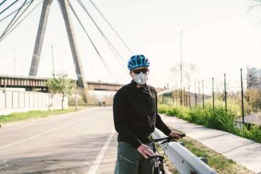 Solunum maskesi takan ve ağır koruyucu filtresi olan bir erkek bisikletçi. Bisikletli bir adam solunum maskesi takıyor ve ağır koruma filtresi takıyor. Güvenli nefes alma maskeleri. Kirlilik kavramı.
