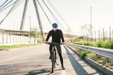 Motosikletli, N95 maskeli, üstü örtülü bir şehirde. Hava kirliliği. Endüstriyel şehir. Tozdan maskeli adam. Solunum cihazındaki adam 2.5 temalı Covid 19. Sis, kirlenmiş zehirli hava, solunum hastalıkları.