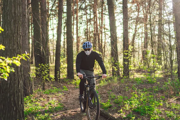 Cyclist wearing pollution mask. Young guy in respirator with filter pm 2.5 with ride on bike in park. Covid 19 Quarantine Sport. Mountain biker riding cycling in forest. mountainbiker on a trail.