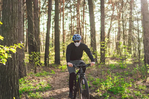 Sport. Mountain Bike cyclist riding single track. Man on bike wearing respirator face mask with heavy duty protective filter. Safety breathing masks. Pollution concept. Riding mountain bike in forest.