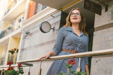 Yaz tatili için Avrupa 'da bir ev kiralama konusu. Elbise giymiş genç beyaz bir kadın çiçeklerle süslenmiş bir apartman dairesinde poz veriyor. Otelin yanındaki kız.
