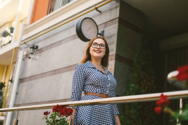 Kiralık daireler. Tatil Avrupa Seyahat Turizmi. Elbiseli bir kız, küçük, rahat bir Avrupa otelinin girişinde duruyor. Terasta duran güzel kadın. Balkonda mutlu bir kadın