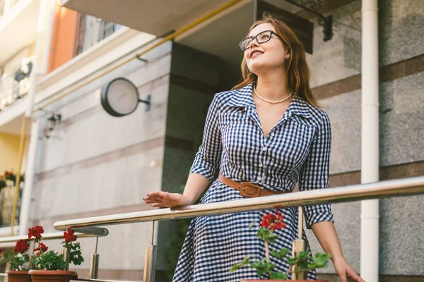 El tema del alquiler de una casa en Europa para las vacaciones de verano. Una joven mujer caucásica en un vestido posa en una terraza de apartamentos decorados con macetas con plantas. Chica cerca del hotel — Foto de Stock