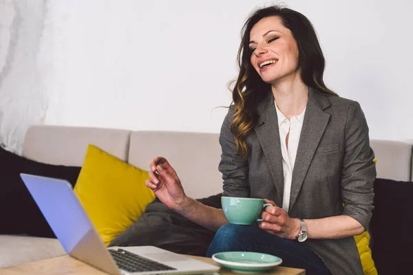 Modern business woman with Cup coffee in workplace. Businesswoman with laptop at cafe. Coffee break for middle-aged lady in office clothes drinks hot drink while working at computer in coffee shop.