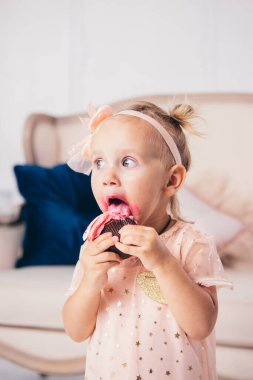 Çocukların doğum günü. İki yaşında, pembe elbiseli komik bir beyaz kız. Evin yatak odasında duruyor. Kanepenin arkasında yemek yiyor, elinde pasta tatlısı tutuyor. Yüzü ve ağzı krem bulaşmış..