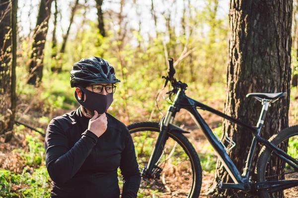 Young woman in protective mask from environmental pollution riding mountain bike on forest road. Cyclist Riding Bike on Trail in park. Face pollution mask smog dust protection. Coronavirus Covid 19.