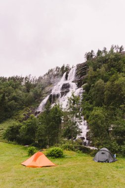 Norveç 'te Voss yakınlarındaki Tvindefossen şelalesinin arka planında Tvinde kamp çadırları var. Norveç fiyortlarında kamp yeri.