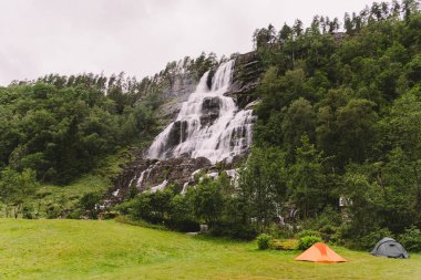 Norveç 'te Voss yakınlarındaki Tvindefossen şelalesinin arka planında Tvinde kamp çadırları var. Norveç fiyortlarında kamp yeri.