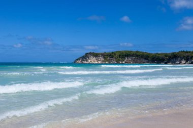 Kumlu sahil manzarası, beyaz köpük dalgaları, palmiye ağaçları, mavi gökyüzü, turkuaz su ve bulutlar, Dominik Cumhuriyeti 'nin cennet kıyıları. 