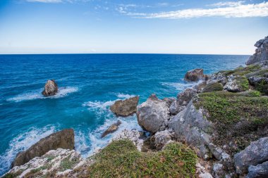 Karayipler kıyısında yeşil orman kayaları ve Dominik Cumhuriyeti 'nde dramatik bulutlarla dolu bir uçurum manzarası.