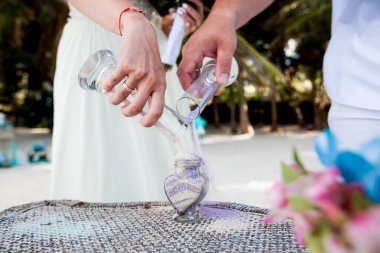 Gelin ve damat, Dominik Cumhuriyeti 'nin Punta Cana kentindeki okyanusun önündeki kumlu sahil nikah töreninde kristal vazoya renkli farklı renkte kumlar döküyorlar.