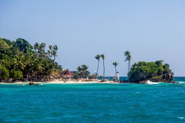 Dominik Cumhuriyeti 'nde palmiye ağaçları, kumlu plajlar, yeşil dağlar, kayalar, mavi gökyüzü ve turkuaz su ile Karayip manzarası 