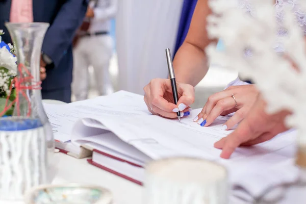 Bride signing wedding marriage certificate with pen on outdoor wedding ceremony