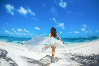 Tropikal Karayip kumlu plaj manzarasında turkuaz deniz ve mavi gökyüzü ile güneşli günün tadını çıkaran bir kadın. 
