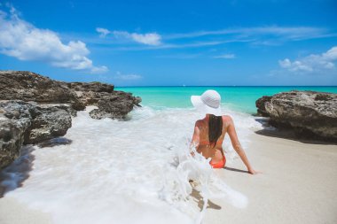 Tropikal Karayip kumlu plaj manzarasında turkuaz deniz ve mavi gökyüzü ile güneşli günün tadını çıkaran bir kadın. 
