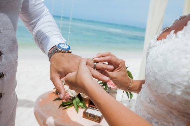 Gelin ve damat, Dominik Cumhuriyeti, Punta Cana 'da okyanusun kıyısındaki kumsalda deniz manzaralı düğün sırasında yüzüklerini değiş tokuş ediyorlar.  