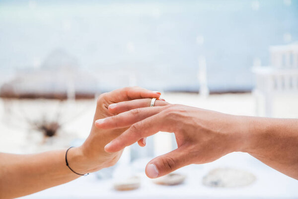 Bride and groom exchanging wedding rings close up during symbolic nautical decor destination wedding marriage on sandy beach in front of the ocean in Punta Cana, Dominican republic  