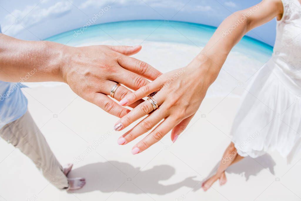 Bride and groom exchanging wedding rings close up during symbolic nautical decor destination wedding marriage on sandy beach in front of the ocean in Punta Cana, Dominican republic  