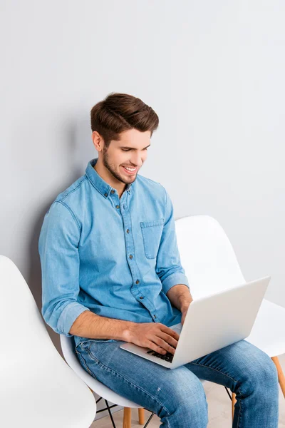 Jovem feliz sentado na cadeira e usando laptop — Fotografia de Stock