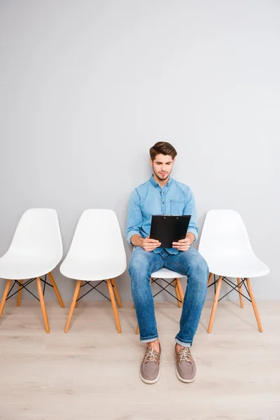 Porträt eines Mannes, der auf einem Stuhl sitzt und seinen Lebenslauf im Faltblatt liest — Stockfoto