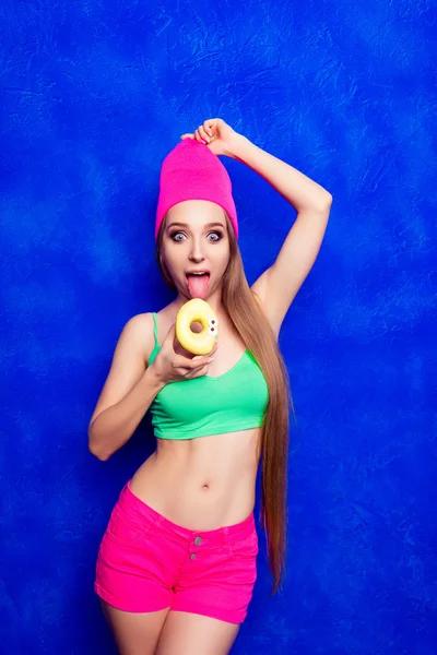 Retrato de mulher bonita cômica em chapéu rosa comendo donut — Fotografia de Stock
