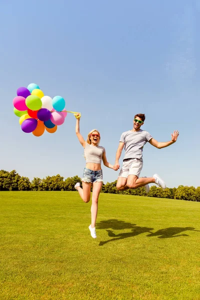 Happy man and woman holding balloons and jumping in the park