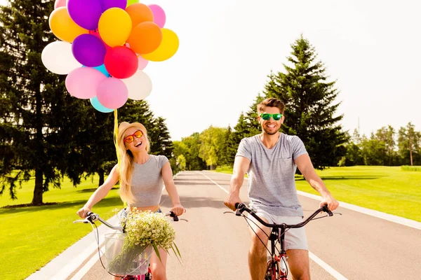 Feliz homem alegre e mulher andar de bicicleta com balões — Fotografia de Stock