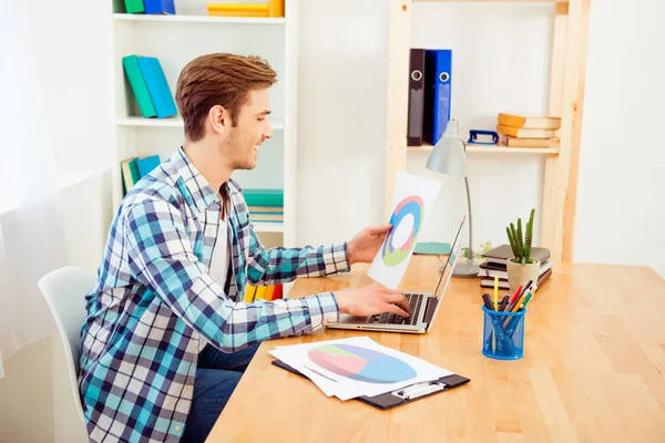 Zijaanzicht van gelukkige werknemer houden diagrama en typen op laptop — Stockfoto
