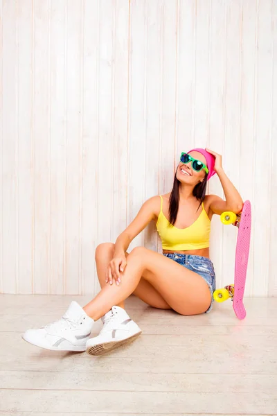 Mulher feliz em boné rosa e óculos sentados no chão com longbo — Fotografia de Stock