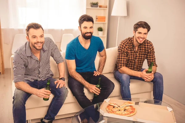 Портрет красивых друзей, сидящих на диване с пивом и пиццей — стоковое фото