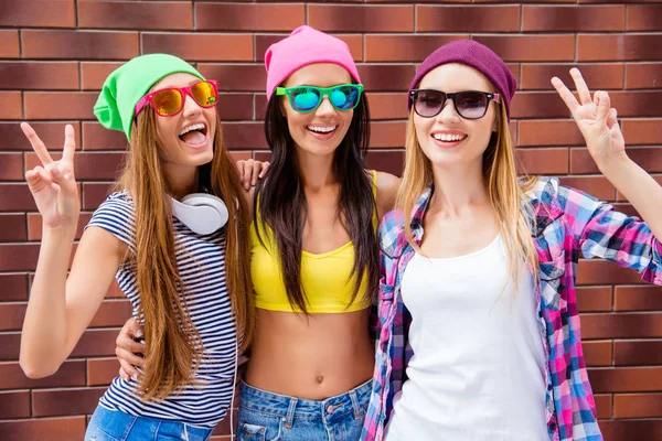 Cheerful girlfriends in hats and glasses gesturing with two fing — Stock Photo, Image