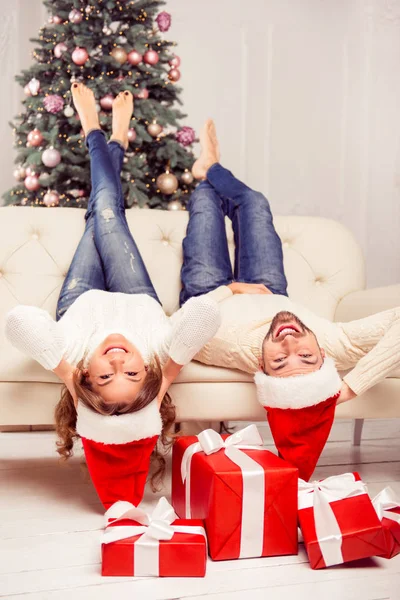 Twee geliefden in santa hoeden liggend op de Bank met verhoogde benen — Stockfoto