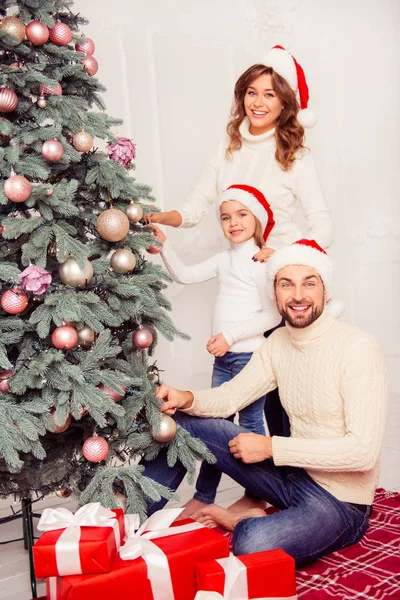 Gelukkige familie in santa hoeden kerstboom versieren — Stockfoto