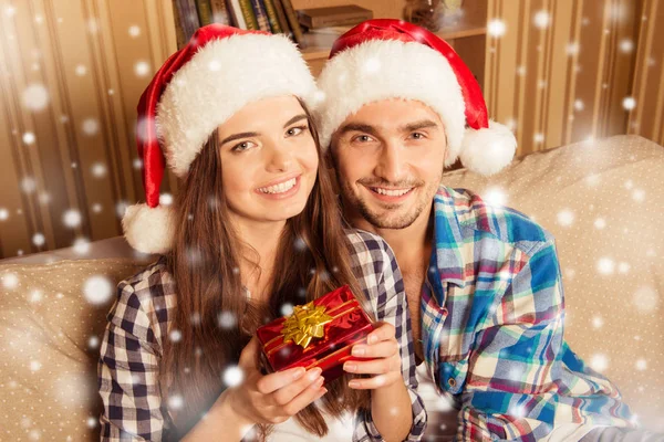 Feliz pareja joven en sombreros de santa celebración de un regalo de Navidad — Foto de Stock