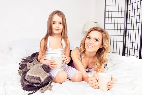 Portrait de maman et fille couchées au lit avec des tasses de lait chaud — Photo