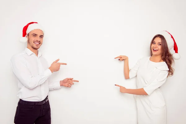 Šťastné veselé muž a žena v červené santa klobouky směřující na každém — Stock fotografie